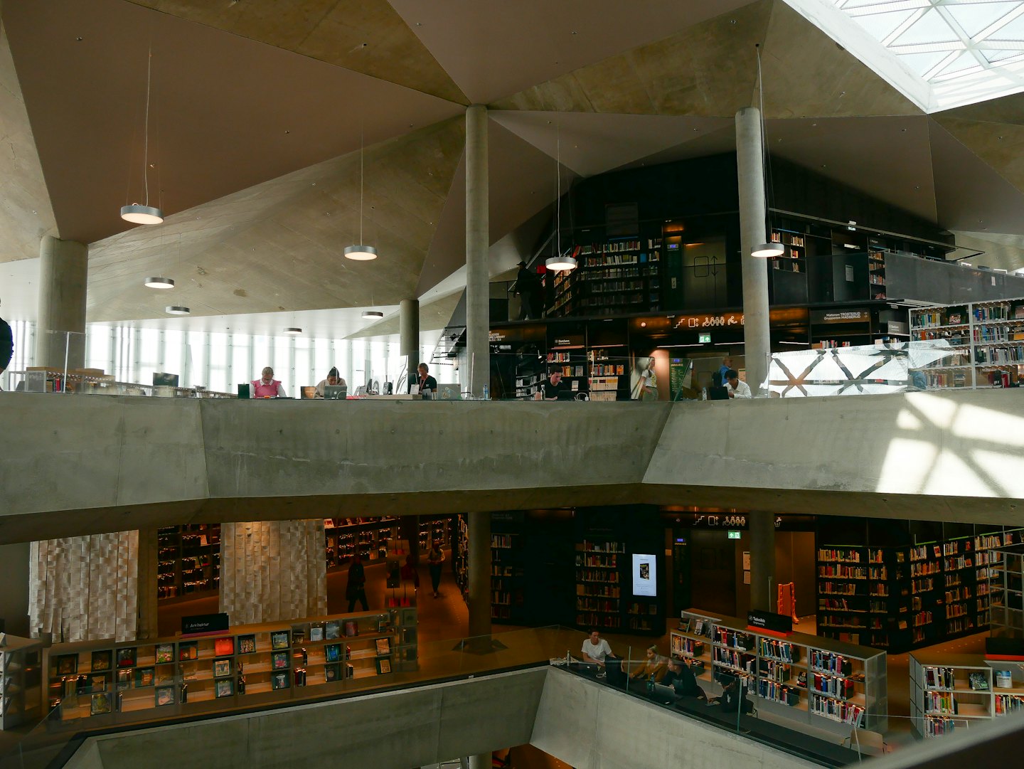 Gente trabajando en portátiles dentro de una biblioteca de hormigón de varios niveles.