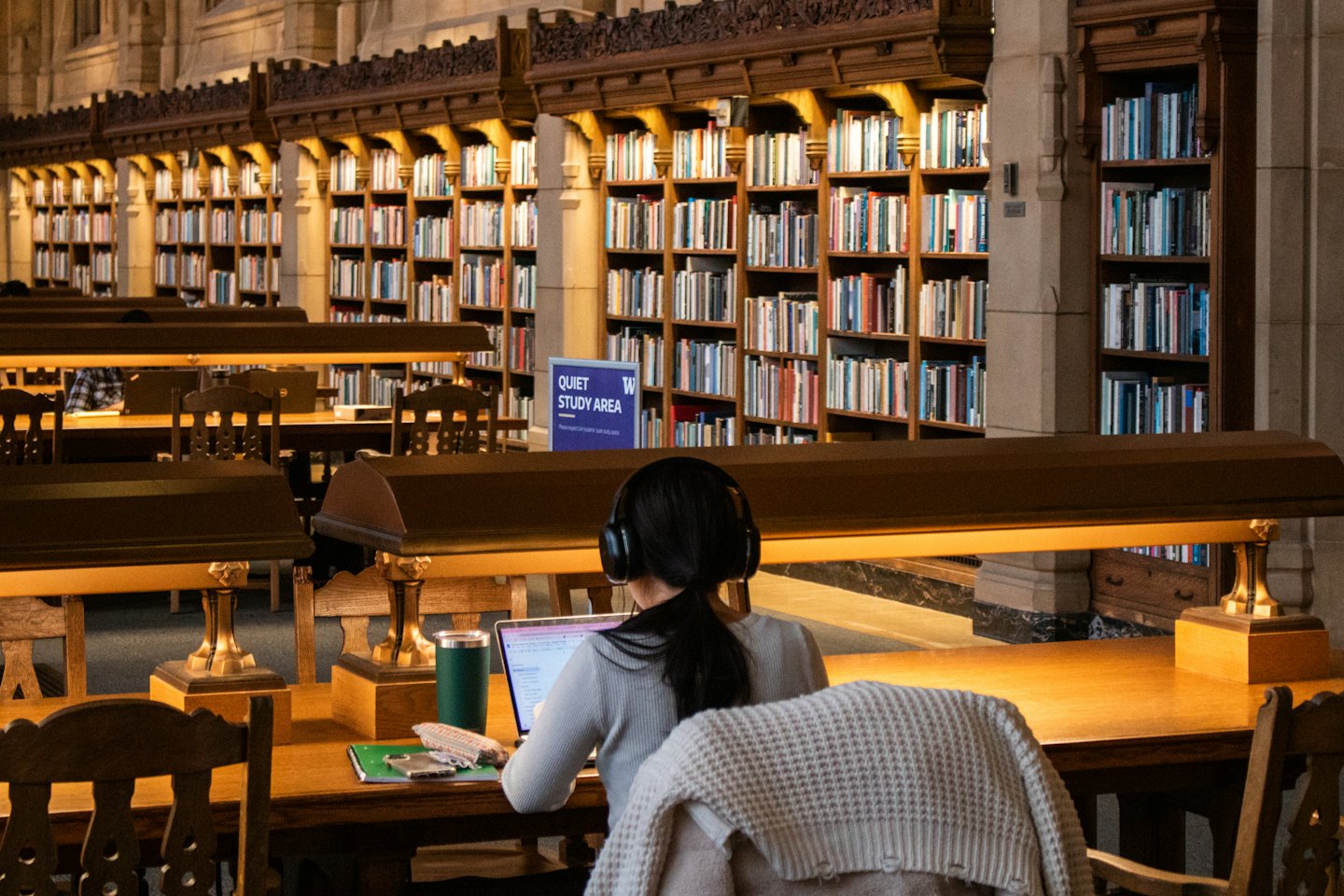 Persona con auriculares trabaja en un portátil en un escritorio de madera en una biblioteca.