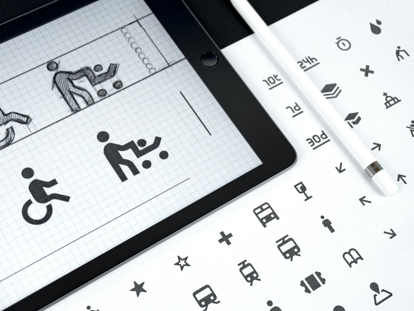 Una tableta muestra conceptos de diseño gráfico junto a un lápiz óptico y una hoja de iconos.