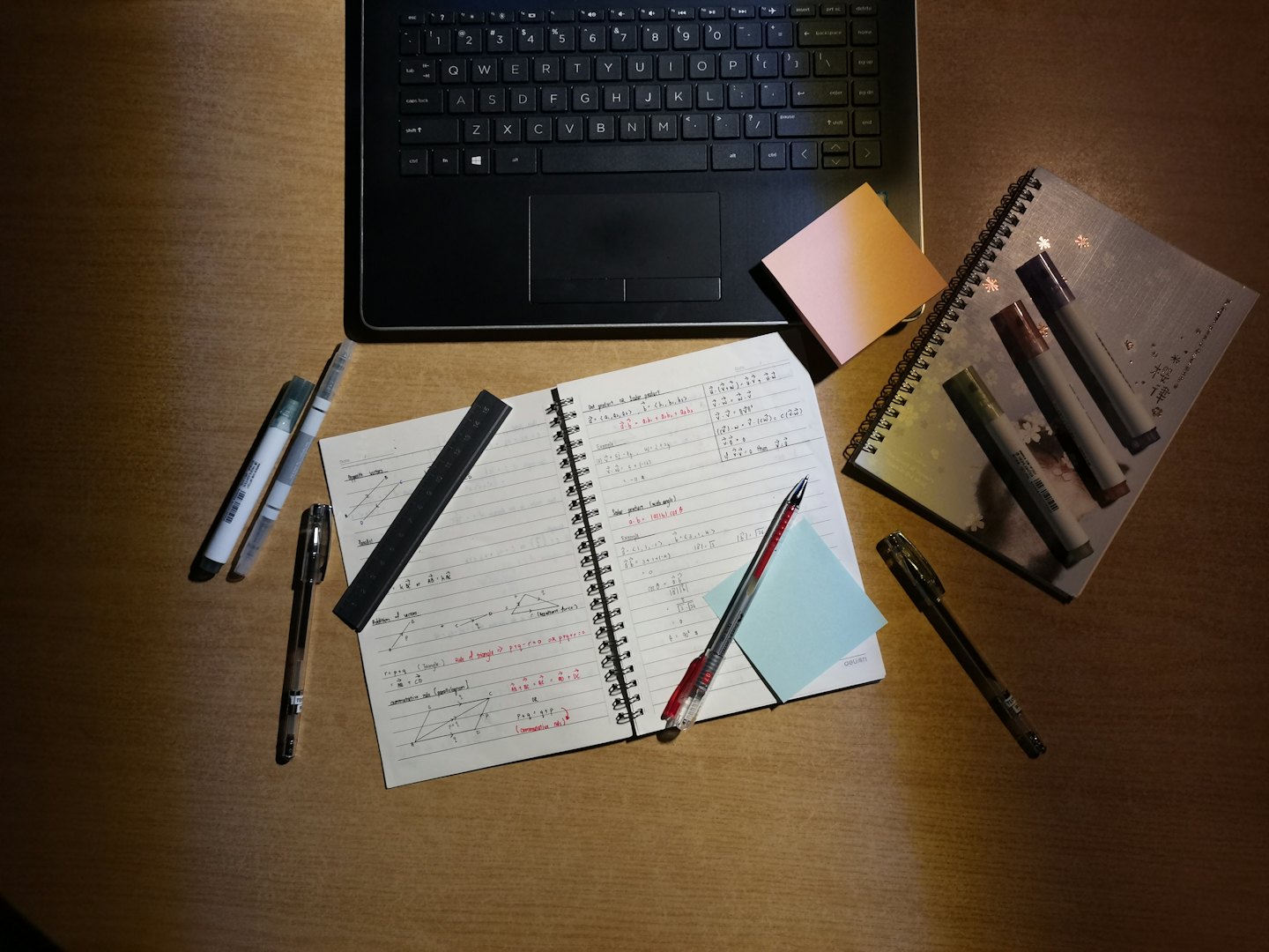 Portátil abierto y cuaderno de matemáticas sobre un escritorio de madera.