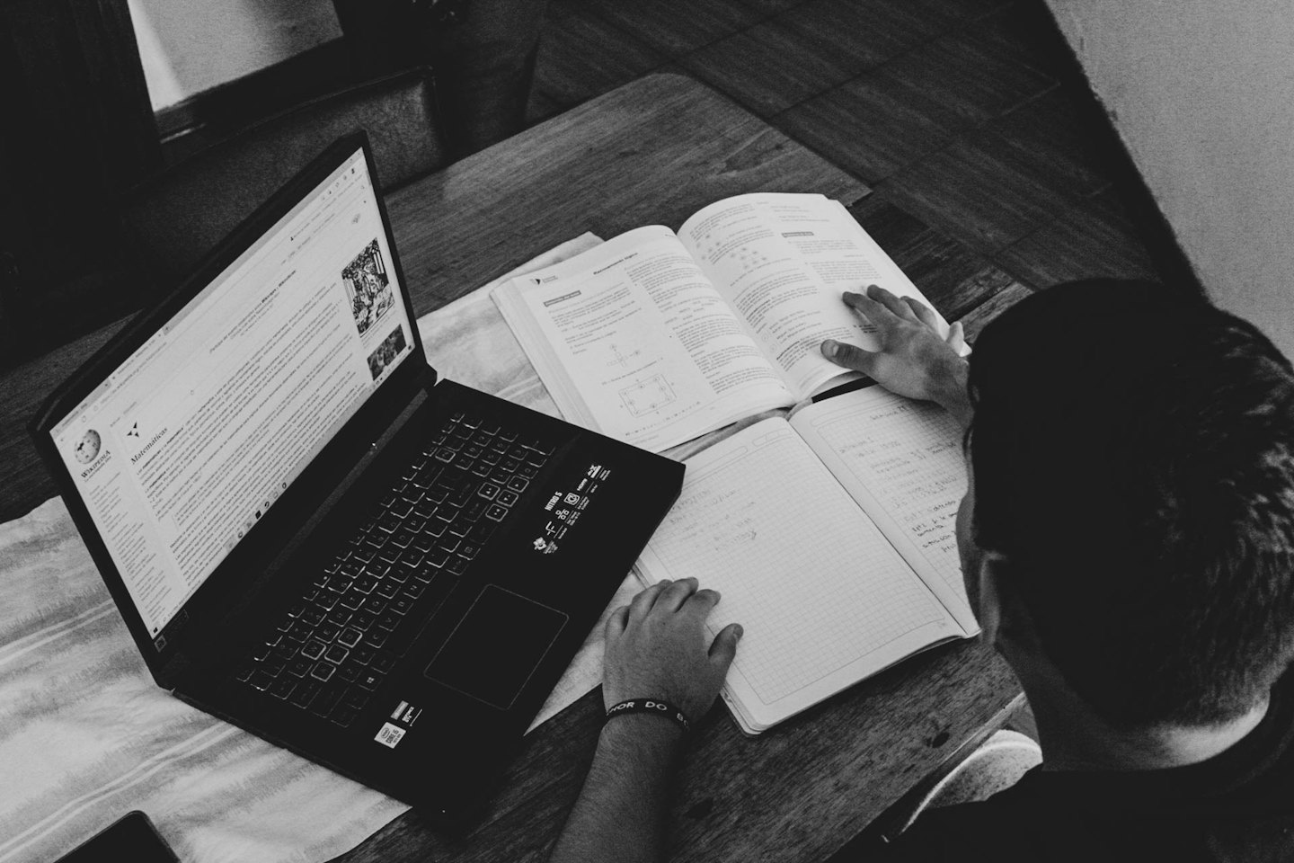 Estudiante estudiando en un escritorio de madera con portátil y libro de texto.